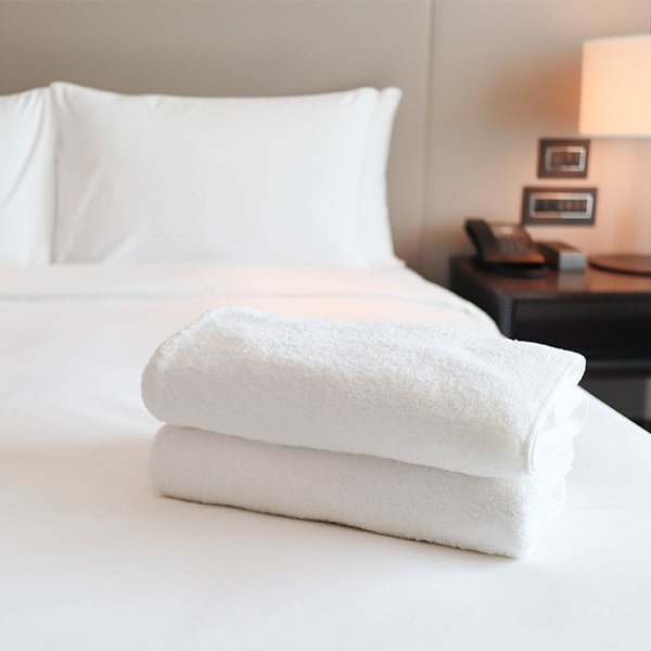 Linge hôtelier N'Clean plié avec soin sur un lit, serviettes blanches impeccables